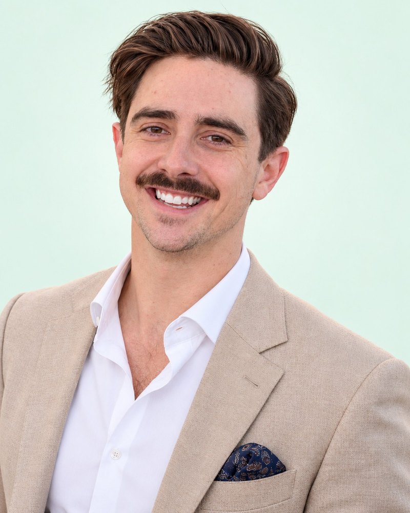 Theo Halbardier, smiling, in a tan blazer and white shirt against a soft mint background.
