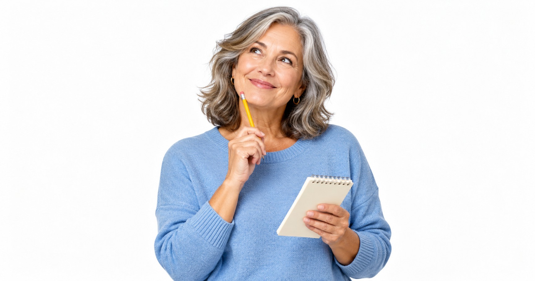 A woman in her late fifties with a pencil and notepad, smiling thoughtfully against a white background.